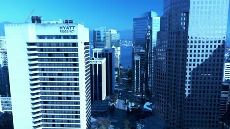 Vancouver-downtown-aerial-drone-dolly-roll-overlooking-quiet-rush-hour-Burrard-Dunsmuir-to-West-Georgia-office-hotel-towers-public-transit-station-bright-sunny-day-post-COVID-lush-green-city-trees-5-5