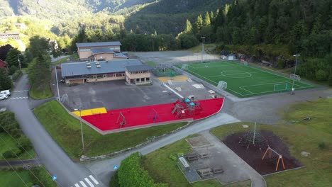 Many-kids-playing-inside-Stanghelle-schoolyards-ball-pit---Aerial-outside-schoolyard-premises-looking-towards-children-and-building---Vaksdal-Norway