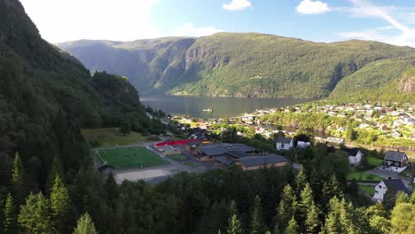 Stanghelle-school-seen-from-behind-forest-trees-with-beautiful-fjord-and-mountain-background---Forward-moving-aerial-Norway