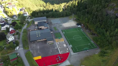 Stanghelle-elementary-school-in-Vaksdal-Norway---High-altitude-aerial-looking-down-at-building-surrounded-with-colorful-playground-and-football-field-with-kids
