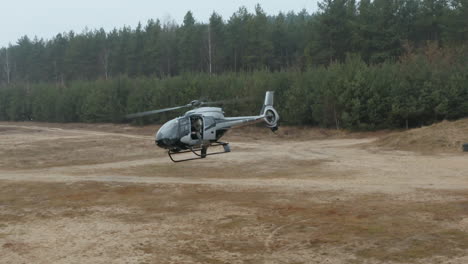 Drone-Shot-of-Military-Helicopter-With-Solder-on-Cockpit-Door-Flying-Above-Training-Field
