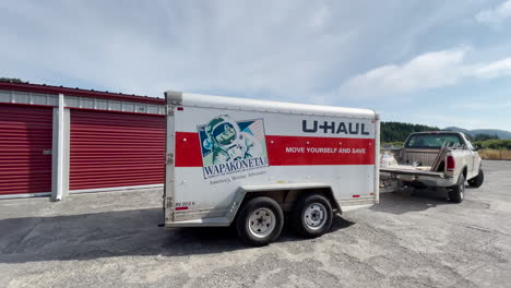 Man-in-Ford-truck-drives-away-from-storage-shed-with-U-Haul-trailer-in-tow