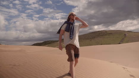 European-tourist-wearing-sun-shades-walks-across-sand-dunes-on-the-shore-of-the-Atlantic-Ocean