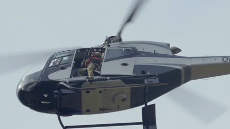 Helicóptero-Militar-Volando-Con-Soldado-Armado-Y-Rifle,-Entrenamiento-De-Fuerza-Especial,-ángulo-Bajo