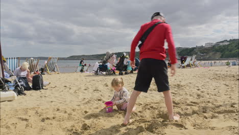 Brother-and-sister-playing-in-the-sand-on-the-beach-little-girl-filling-a-bucket-with-sand-Scarborough-UK