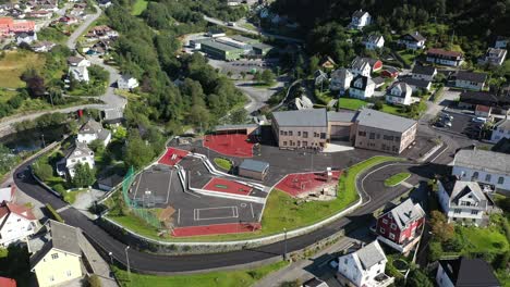 Modern-new-Vaksdal-elementary-schol-and-schoolyard-with-playground---Orbiting-aerial-with-tilt-up-to-reveal-surroundings-and-fjord-background