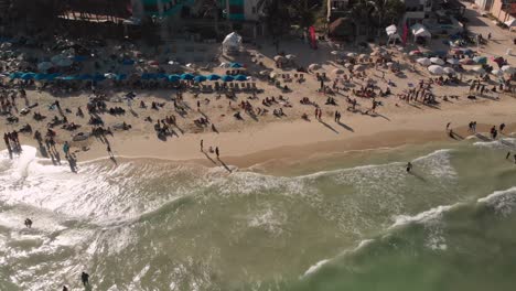 High-angle-ascending-footage-of-crowded-beach-in-tropical-travel-destination-at-golden-hour