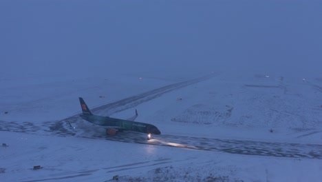 Boeing-Airplane-taxiing-on-snow-covered-tarmac-during-winter-conditions,-aerial