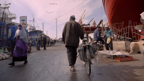 Hombre-Marroquí-Camina-Junto-A-Su-Bicicleta-En-La-Ciudad-Portuaria-De-Essaouira,-Marruecos