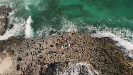 People-visiting-rocky-sea-cliff-surrounded-by-dangerous-waves-in-Mexico,-aerial-tilt-up