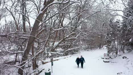Aerial-shot-of-an-older-couple-walking-through-a-snow-covered-park