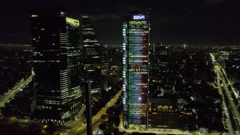 Aerial-view-around-the-BBVA-tower-illuminated-in-the-colors-of-the-Mexican-flag,-Independence-day-in-Mexico-city---circling,-drone-shot