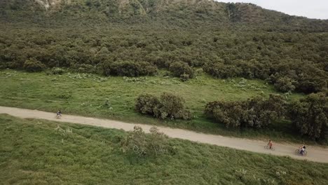 Orbital-drone-view-of-group-of-cyclists-riding-along-a-dirt-road-near-Lake-Naivasha,-Kenya,-Africa
