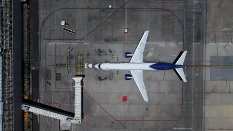 Aerial-view-of-terminal-workers-assisting-a-plane-at-departure---Birds-eye,-drone-shot