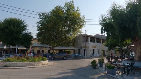 Cars-drive-in-the-roundabout-in-village-Kassiopi-on-the-island-Corfu,-people-in-the-cafe