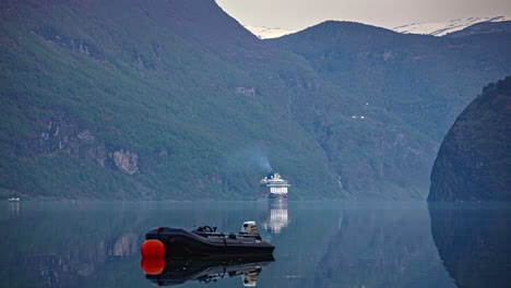 Time-lapse-shot-of-Cruise-Ship-cruising-on-Fjord-between-mountains-in-Norway---Small-Boat-anchored-on-shoreline
