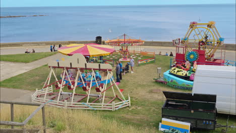 Small-amusement-park-on-seafront-promenade-with-swings,-carousels-and-ferris-wheel-on-a-bright-summers-day-in-Scarborough-August-2022