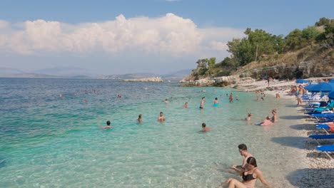People-on-the-beach-bathing-and-swimming,-couple-is-lying-on-the-sandy-beach-in-Kassiopi-on-the-island-Corfu