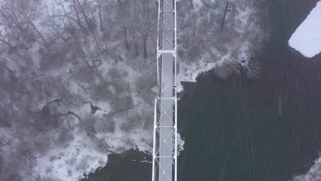 Overhead-aerial-view-of-a-train-bridge-going-over-a-river-with-snow-everywhere