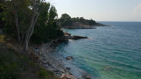 People-sunbathe-and-dive-on-the-wild-rocky-beach,-coastline-of-island-Corfu,-village-Kassiopi,-Greece