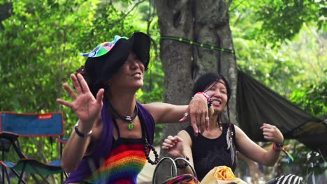 Two-Asian-women-dresses-in-hipster-style-clothing-rotating-hands-in-circular-motion-during-ecstatic-dance-performance-with-outdoor-scenery,-filmed-as-medium-close-up-in-slow-motion