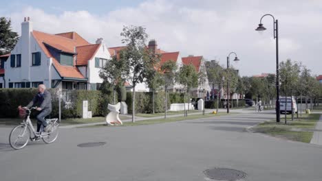 Senior-man-biking-along-the-residential-houses-in-the-famous-Concession-quarter-in-De-Haan,-Belgium