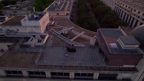 Aerial-drone-shot-of-videographer-filming-music-video-with-DJ-disk-jockey-on-roof-of-high-rise-buildings-at-sunset---France,Montpellier