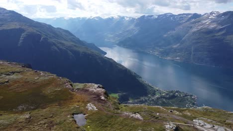 Breathtaking-aerial-view-from-dronningstien-queens-hiking-trail-with-Lofthus-village-far-down-below-steep-cliff---Friends-resting-at-cliffs-edge---Revealing-fjord-view-with-parallax-effect