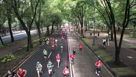 Rückwärtsdrohnenaufnahme-Von-Marathonläufern-In-Mexiko-Stadt,-Die-Die-Mexikanische-Flagge-Tragen