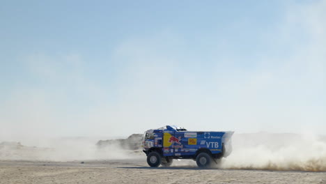 Großer-Dakar-rallye-truck,-Der-An-Einem-Sonnigen-Tag-Mit-Wolken-Aus-Staubigem-Goldenem-Sand-Vorbeifährt