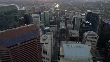 Flying-in-middle-of-high-rise-in-downtown-Calgary,-during-sunset---Aerial-view