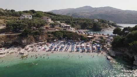Reversing-aerial-view-of-bataria-beach-on-Kassiopi,-Corfu,-people-bathe-and-rest-on-vacation