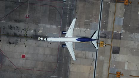 Pushback-tug-vehicle-assisting-a-airplane-at-departure---top-down,-aerial-view