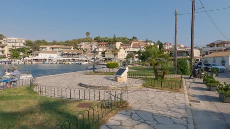View-of-the-monument-and-promenade-in-Kassiopi,-people-sitting-on-the-bench-on-seashore
