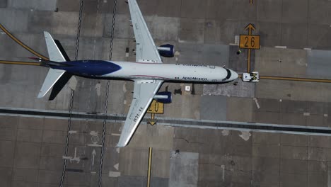 Aerial-view-of-a-Aeromexico-Boeing-757-200-plane-getting-pushed-at-a-airport---descending,-tilt,-drone-shot