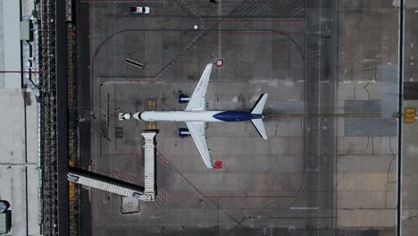 Vista-Aérea-Del-Equipo-De-Mantenimiento-Que-Trabaja-En-Un-Avión-En-Una-Terminal-Del-Aeropuerto---De-Arriba-Hacia-Abajo,-Disparo-De-Drones