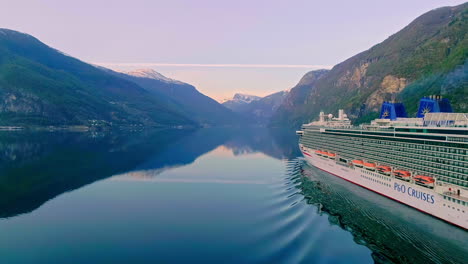 Aerial-drone-shot-of-giant-P-and-O-cruise-ship-sailing-in-Norwegian-Fjord-in-Flam,-Norway-with-mountain-range-on-both-sides-at-daytime