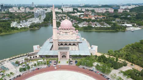 Toma-Aérea-De-Paralaje-De-La-Mezquita-Putra-Rosa-Sobre-El-Agua-En-Putrajaya-Malasia