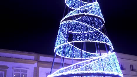 Tiro-Ascendente-En-Cámara-Lenta-De-Cono-Luminoso-Decorado-Con-Una-Estrella-Luminosa-En-La-Parte-Superior-Para-Navidad-Por-La-Noche-En-Una-Luz-Blanca-Azul