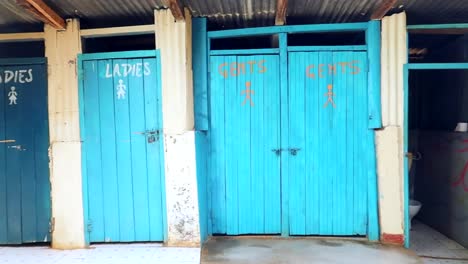 Vista-Del-Baño-Turístico-Con-Puertas-Azules-Brillantes-Marcadas-Damas-Y-Caballeros-En-Un-área-De-Kenia,-África