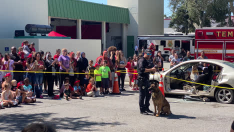 A-police-officer-talking-to-a-crowd-of-adults-and-kids-at-a-public-demonstration-with-a-police-dog-that's-trained-to-assist-police-and-other-law-enforcement-officers