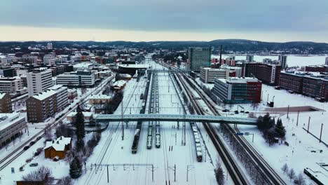 Aerial-view-of-trains-at-the-railway-station-in-Jyvaskyla,-cloudy,-winter-evening-in-Finland---descending,-drone-shot