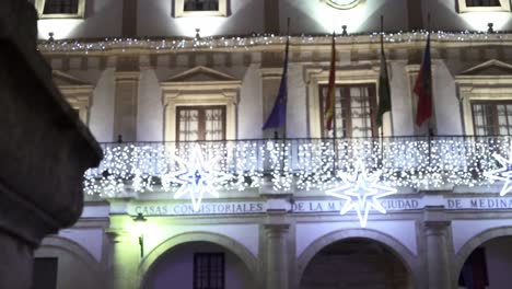 Zeitlupenschwenk-über-Die-Säule-Einer-Mauer-Während-Der-Kamerafahrt-Das-Rathaus-Casa-Consistorial-Von-Medina-Sidonia-In-Cadiz-In-Spanien-Mit-Geschmücktem-Balkon-Mit-Lichtern-Und-Weihnachtselementen