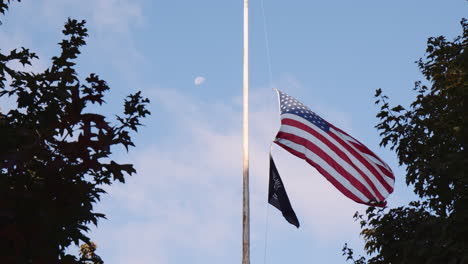 Bandera-Estadounidense-A-Media-Asta-Ondeando-Junto-Al-Emblema-Oficial-De-La-Liga-Nacional-De-Familias-Pow-Mia-Flag-En-Central-Park,-Vista-De-ángulo-Bajo-A-Través-De-árboles,-Día-Conmemorativo
