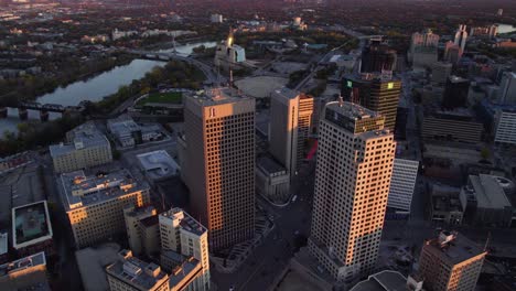 Aerial-view-around-sunlit-high-rise-in-downtown-Winnipeg,-sunset-in-Manitoba,-Canada---circling,-drone-shot