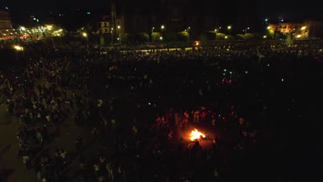 Aerial-view-over-protesters-having-a-bonfire-on-a-large-city-square---tilt,-drone-shot