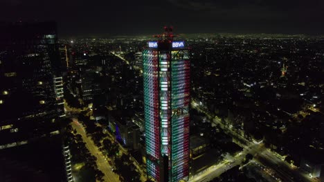 Aerial-view-towards-the-BBVA-tower-illuminated-in-the-colors-of-the-Mexican-flag,-Independence-day-night-in-Mexico-city