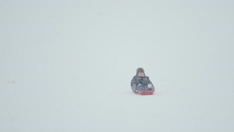 Kid-sliding-down-the-side-of-a-mountain-with-a-lot-of-snow-actively-falling