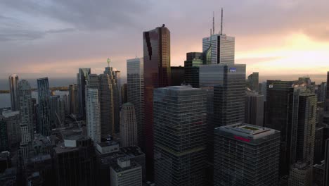 Aerial-view-in-front-of-skyscrapers-in-downtown-Toronto,-sunset-in-Ontario,-Canada---pan,-drone-shot