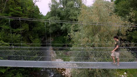 Joven-Caminando-Sobre-Un-Puente-Colgante-Tibetano-En-La-Naturaleza-Salvaje-Sobre-El-Río,-Turín,-Italia